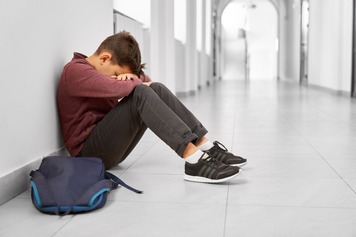 niño con trastorno disocial sentado en el pasillo del colegio, solo y con las manos tapándose la cara